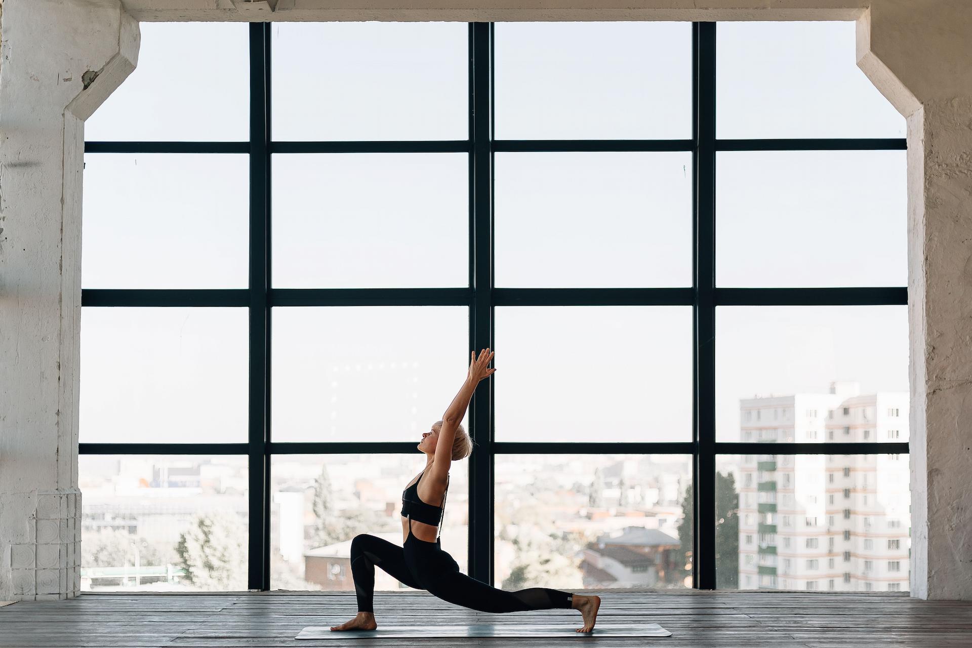 A woman doing yoga next to a large window.