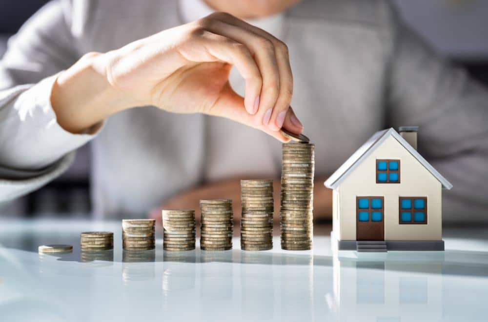 Person Counting Coins Toward Toy House On Desk