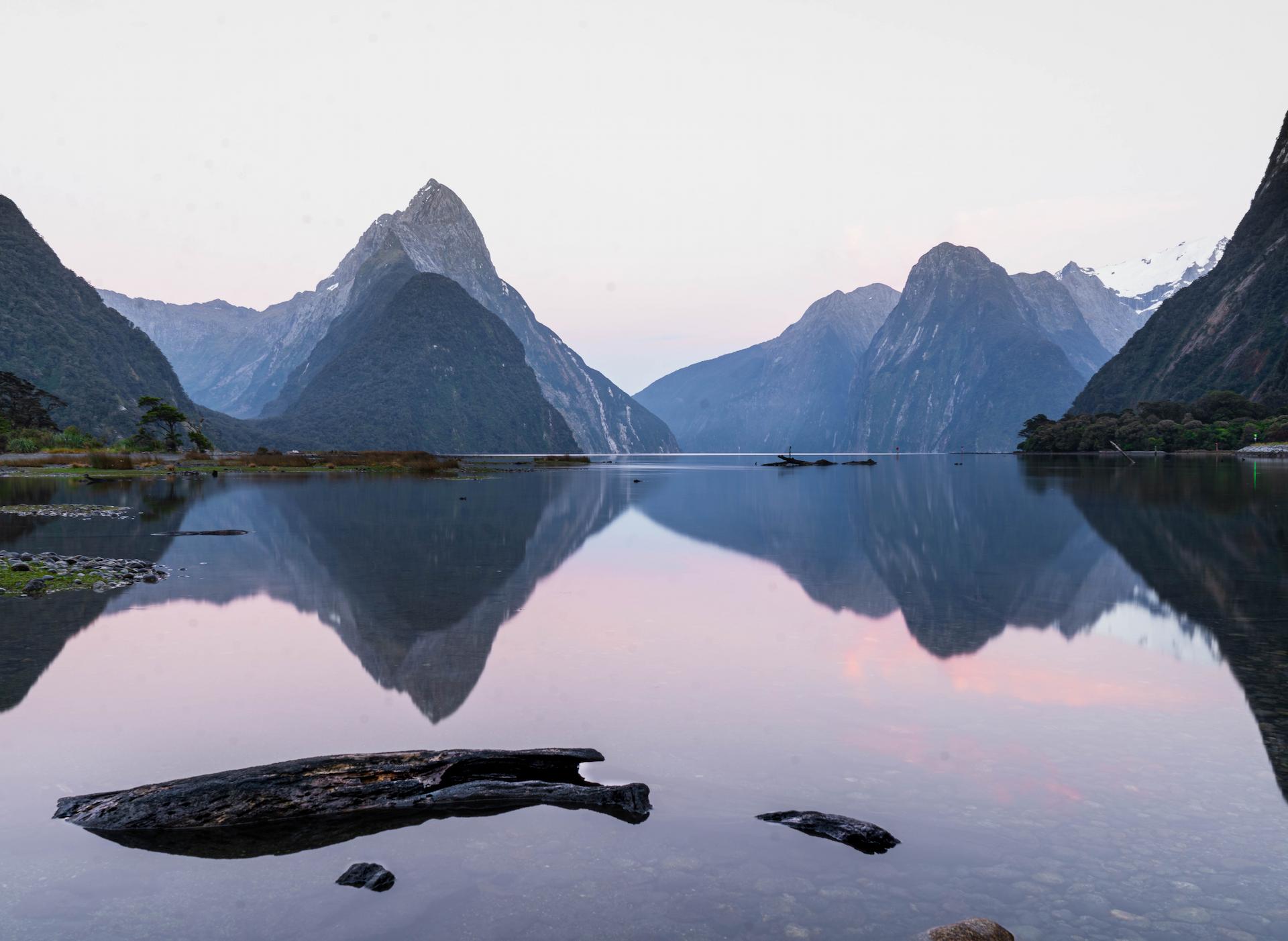 In Milford Sound, Te Anau, New Zealand, the water reflects the large mountains behind it.